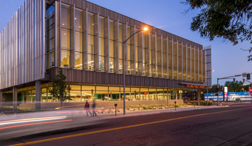 Modern building with large glass windows, illuminated at dusk, located on a city street.