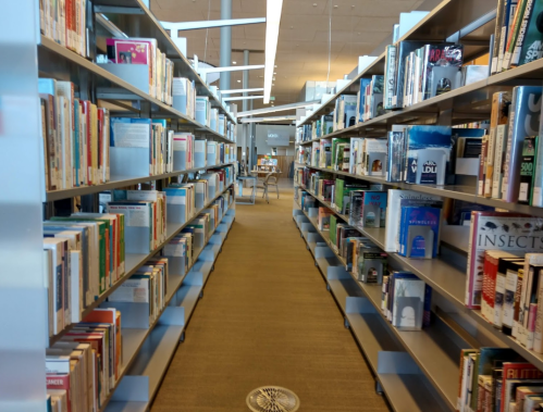 A view of a library aisle lined with bookshelves, leading to a study area in the background.