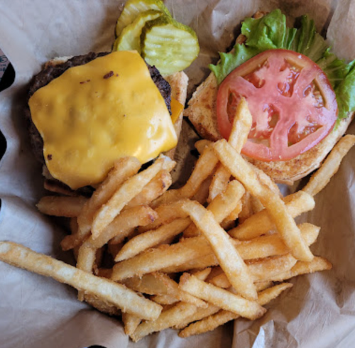 A cheeseburger with lettuce, tomato, and pickles, served with a side of golden French fries on a paper-lined tray.