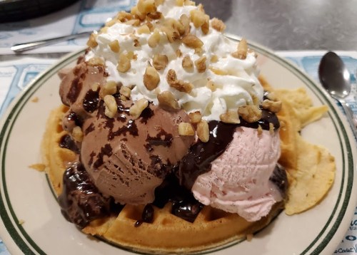 A delicious waffle topped with chocolate and strawberry ice cream, whipped cream, chocolate sauce, and chopped nuts.