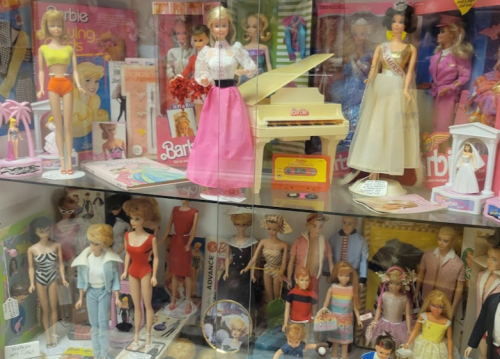 A display case filled with various Barbie dolls, outfits, and accessories from different eras.
