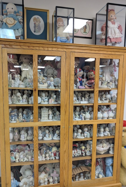 A wooden display cabinet filled with various dolls and figurines, with more dolls showcased in glass cases above.