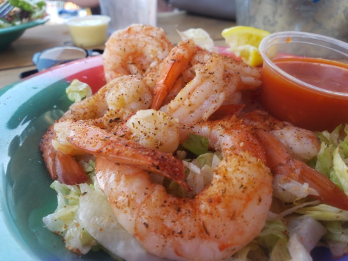 A plate of seasoned shrimp on a bed of lettuce, served with a side of cocktail sauce and a lemon wedge.