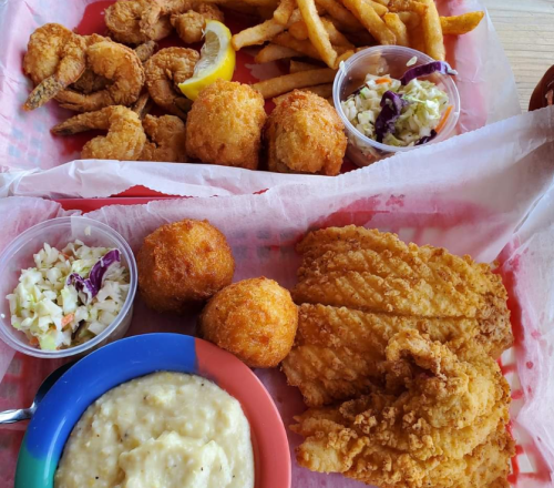A colorful tray of fried shrimp, fish, hushpuppies, coleslaw, fries, and a bowl of grits.