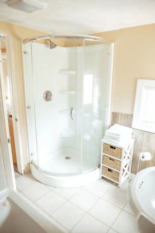 A modern bathroom featuring a glass shower enclosure, white tiles, and neatly stacked towels on a storage unit.
