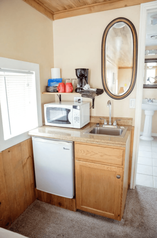 A small kitchenette featuring a sink, microwave, mini fridge, coffee maker, and a mirror on the wall.