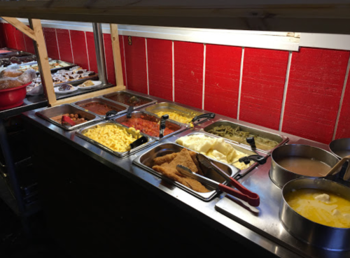 A buffet table with various dishes, including pasta, sauces, and sides, against a red wall.