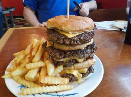A towering burger with multiple patties and melted cheese, served with a side of crinkle-cut fries on a plate.