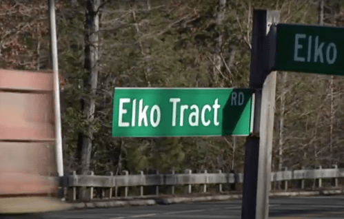 Green street sign for "Elko Tract Rd" with a blurred truck passing by in the background.