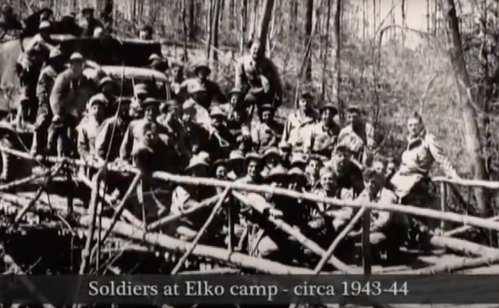 A group of soldiers poses on a wooden structure at Elko camp, surrounded by trees, circa 1943-44.