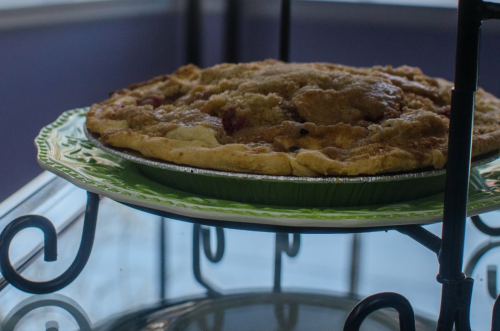 A freshly baked pie on a decorative green plate, displayed on a stand with a blurred background.