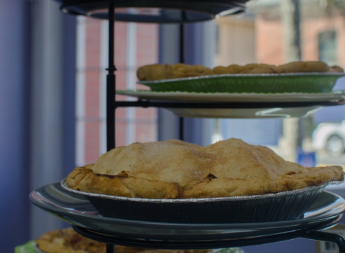 A display of freshly baked pies on tiered stands, showcasing a golden-brown pie in the foreground.