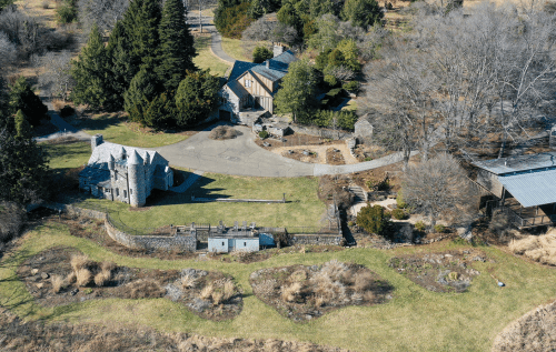 Aerial view of a sprawling estate with stone buildings, manicured lawns, and surrounding trees in a rural setting.