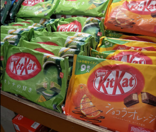 A display of various flavored Kit Kat packages, including green tea and chocolate orange, in a store.