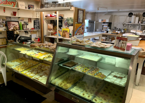A cozy bakery display filled with various pastries and desserts, with a kitchen visible in the background.