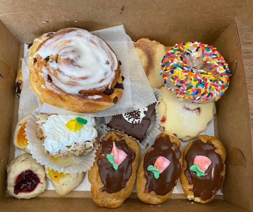 A box filled with assorted pastries, including cinnamon rolls, donuts, and cream-filled treats, all beautifully decorated.