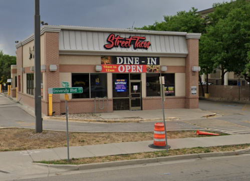 A taco restaurant with a "DINE-IN OPEN" sign, located at the corner of University Blvd, under a cloudy sky.
