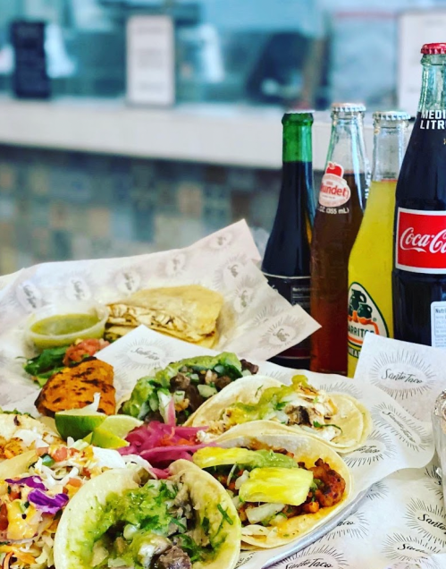 A vibrant spread of tacos with various toppings, accompanied by colorful drinks and sides on a table.