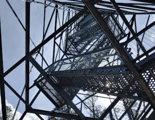 View looking up at a metal tower structure with a spiral staircase and blue sky peeking through.