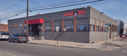 Exterior view of Capital City Antique Mall, a gray building with red accents, located at a street corner.