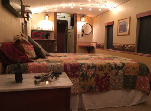 Cozy bedroom with a colorful quilt, string lights, and a small kitchenette area in a warm, inviting space.