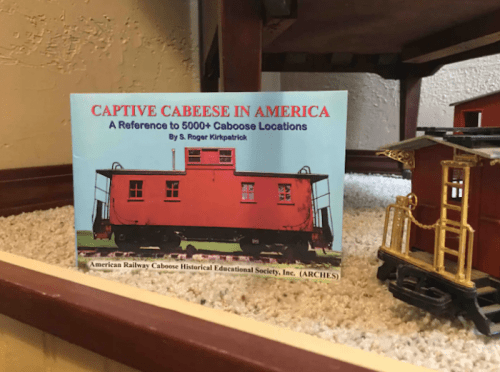 Book titled "Captive Cabeese in America" displayed next to a model train caboose on a shelf.