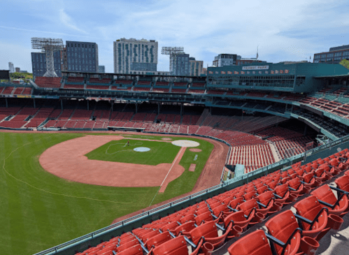 A wide view of a baseball stadium with empty red seats and a green field under a clear blue sky.