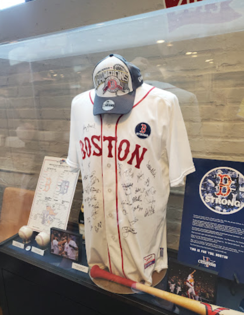 A signed Boston baseball jersey displayed with a cap, memorabilia, and a bat in a glass case.