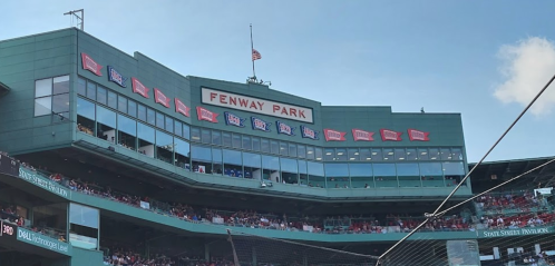 Fenway Park's iconic green facade with flags and a clear blue sky above.