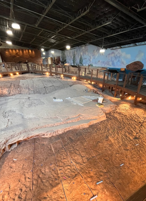 A large, textured geological display with wooden walkways and ambient lighting in a spacious indoor setting.