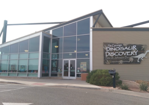 Exterior of the St. George Dinosaur Discovery site at Johnson Farm, featuring large windows and a dinosaur-themed sign.