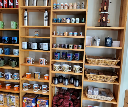 A wooden shelf displaying various mugs, cups, and souvenirs in a store.