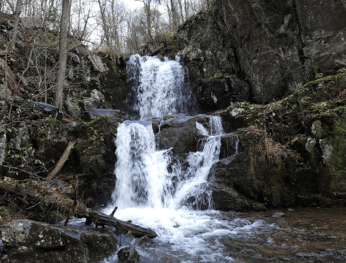 A serene waterfall cascading over rocky terrain, surrounded by trees and natural greenery.