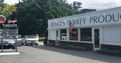 Exterior of Bongi's Turkey Products featuring a sign with menu items and an American flag. Cars parked outside.