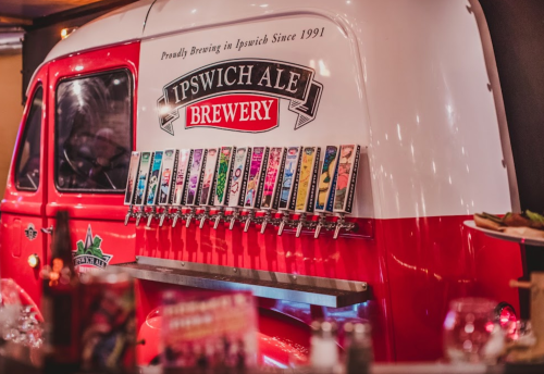 A vintage truck converted into a bar, featuring colorful beer taps and the Ipswich Ale Brewery logo.