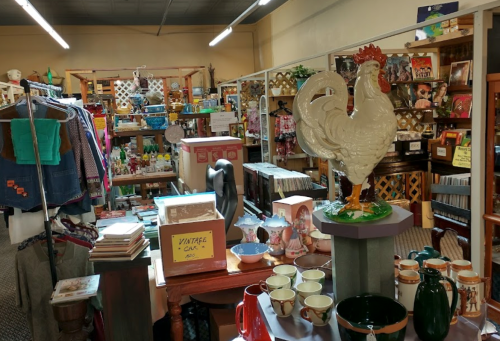 A cozy vintage shop filled with various items, including clothing, decor, and a large rooster statue.
