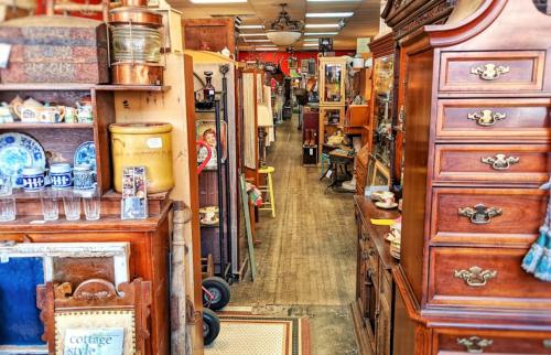 A narrow aisle in an antique shop lined with vintage furniture and collectibles on either side.