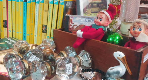 A wooden box filled with vintage items, including glass knobs, elf dolls, and books in the background.