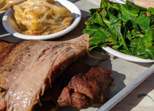 A plate featuring sliced beef, collard greens, and a side of creamy potato dish on a metal tray.