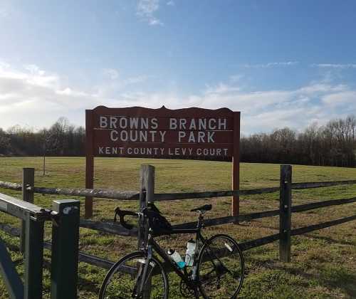 Sign for Browns Branch County Park with a bicycle parked nearby, set against a clear blue sky and grassy field.