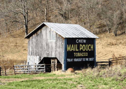 A rustic wooden barn with a large advertisement for "Mail Pouch Tobacco" on its side, surrounded by a rural landscape.