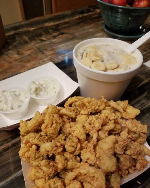 A plate of fried shrimp with two cups of dipping sauce and a cup of banana pudding on a wooden table.