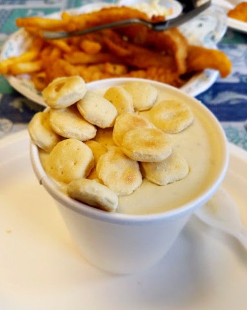 A cup of creamy dessert topped with round cookies, with fries and fried fish in the background.