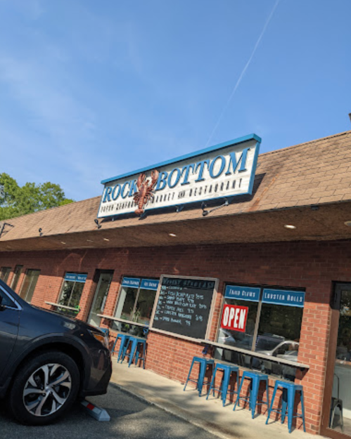 Exterior of Rock Bottom restaurant with a sign, outdoor seating, and an "Open" notice.