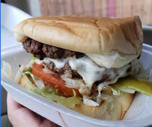 A close-up of a juicy hamburger with lettuce, tomato, mayonnaise, and pickles, served in a soft bun.
