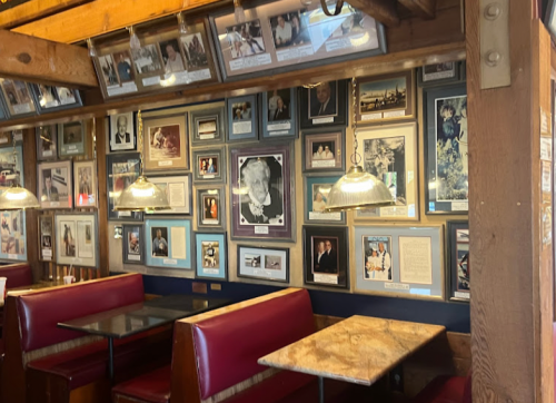A cozy restaurant interior featuring a wall adorned with framed photos and memorabilia, with red booths and pendant lights.