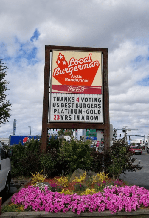 Sign for Local Burgerman featuring a thank you message for voting them best burgers for 23 years, surrounded by flowers.