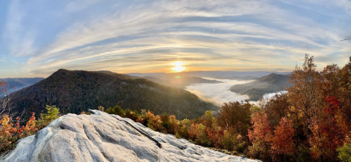 A panoramic view of a sunset over misty mountains, with vibrant autumn foliage in the foreground.