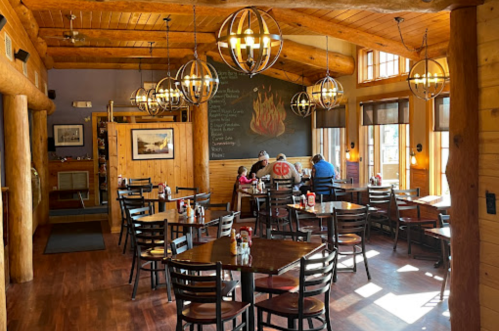 Cozy restaurant interior with wooden decor, pendant lights, and diners at tables. A chalkboard menu is visible.