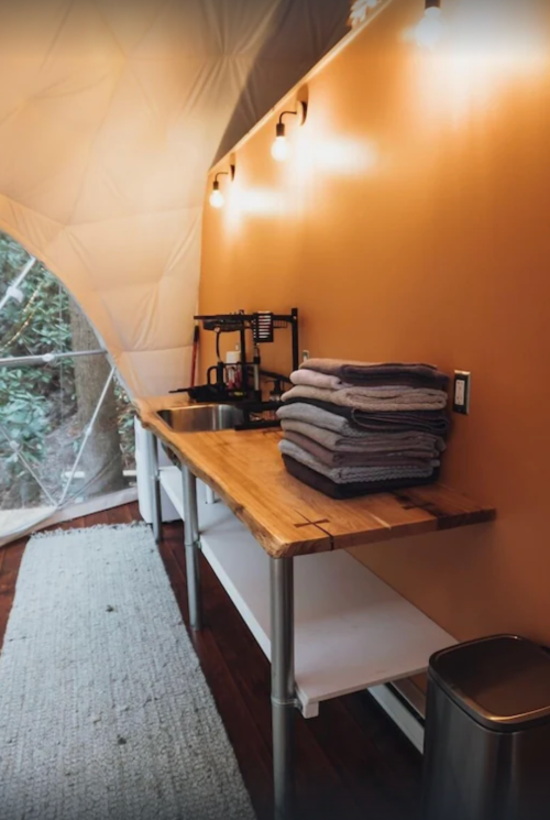 Cozy interior of a glamping tent featuring a wooden table, stacked towels, and warm lighting.